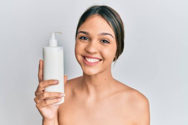 Kozmetik nemlendirici krem tutan genç esmer kadın pozitif ve mutlu görünüyor ve kendine güvenen bir gülümsemeyle dişlerini gösteriyor. 