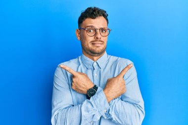 Gündelik kıyafetler giyen ve gözlük takan genç İspanyol adam her iki tarafı da parmaklarıyla işaret ediyor. Farklı yönlere. 