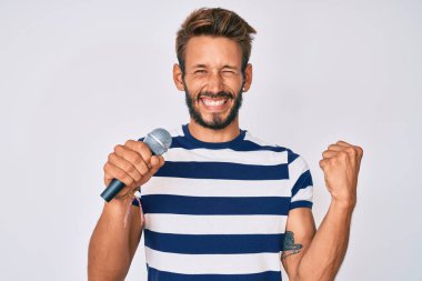 Sakallı yakışıklı beyaz adam mikrofon kullanarak şarkı söylüyor. Gururla bağırıyor, zaferi ve başarıyı kutluyor. 