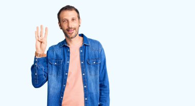 Genç, yakışıklı, günlük kıyafetler giyen, dört numarayı gösteren ve gülümseyen, kendinden emin ve mutlu bir adam.. 