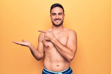 Sakallı, kolsuz tişörtlü, sarı arka planda duran yakışıklı genç adam kameraya hayret ediyor ve gülümsüyordu..