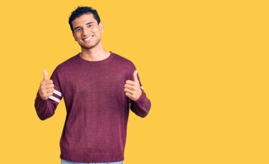 İspanyol asıllı yakışıklı genç adam gündelik kıyafet giyer başarı işareti yapar elle olumlu jest yapar, gülümser ve mutlu olur. Neşeli ifade ve kazanan jest. 