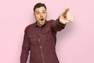 Gündelik giysiler giymiş genç İspanyol bir adam parmağıyla işaret ederek şaşırmış, ağzı açık, şaşırmış, ön tarafta bir şey var. 