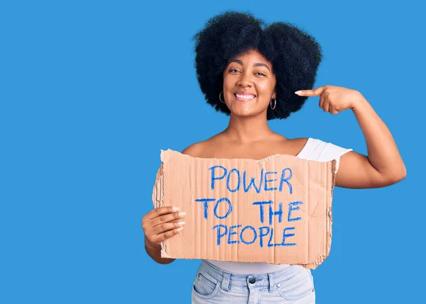 Young african american girl holding power to the people banner pointing finger to one self smiling happy and proud