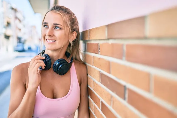 Sarışın Sportif Kulaklık Takan Genç Bir Kız Şehrin Duvarına Yaslanmış — Stok fotoğraf