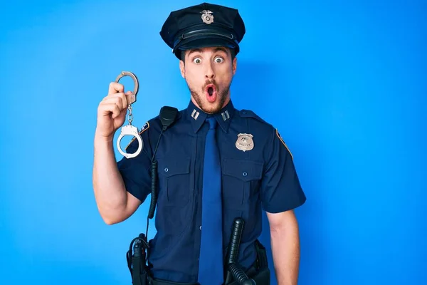 警察の制服を着た若い白人男性が手錠を持って怖がって驚きのために口を開けて驚いて 不信の顔 — ストック写真