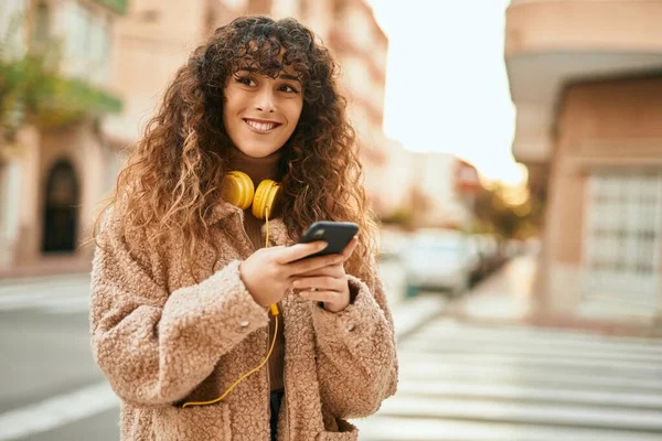 街中でスマホやヘッドフォンを使って笑顔で幸せそうな若いヒスパニック系女性 — ストック写真