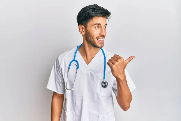 Młody Przystojny Mężczyzna Noszący Mundur Lekarza Stetoskop Skierowany Kciuk Górę — Zdjęcie stockowe