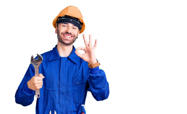 指でOkサインを行う電気技師の制服保持レンチを身に着けている若いヒスパニック系の男 笑顔優しいジェスチャー優れたシンボル — ストック写真