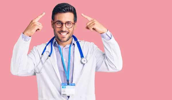 Joven Hombre Hispano Vistiendo Uniforme Médico Estetoscopio Sonriendo Apuntando Cabeza —  Fotos de Stock