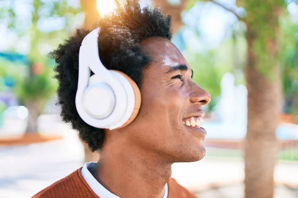 ヘッドフォンを使用して音楽を聴く若いハンサムなアフリカ系アメリカ人男性 町の通りを歩いていると笑顔で立って — ストック写真