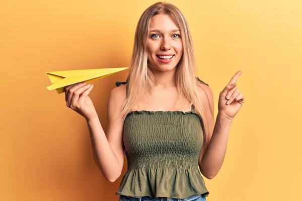 Fiatal Szőke Kezében Papír Repülőgép Mosolyog Boldog Mutató Kézzel Ujjal — Stock Fotó