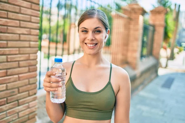 年轻的金发女运动员正在城市里做运动 喝着一瓶水 — 图库照片