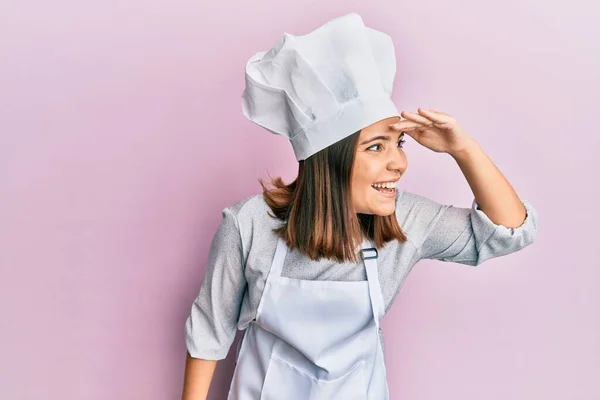 プロの料理の制服を身に着けている若い美しい女性と帽子非常に幸せと笑顔遠くに手を頭の上に見て 検索の概念 — ストック写真