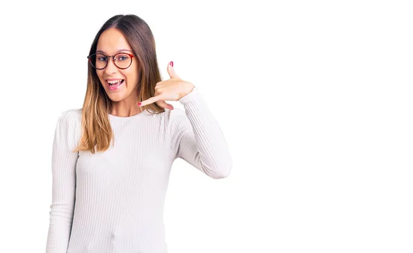 美しいブルネットの若い女性がカジュアルな白いセーターと眼鏡を着て 電話で話すような手や指で電話ジェスチャーをして笑っています コミュニケーションの概念 — ストック写真