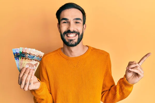 Joven Hispano Sosteniendo Dólares Canadienses Sonriendo Feliz Señalando Con Mano —  Fotos de Stock