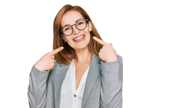 年轻的高加索女人 身穿商务服装 戴着眼镜 笑容满面 用手指 牙齿和嘴指指点点 牙齿健康概念 — 图库照片