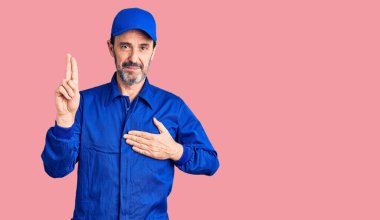 Orta yaşlı, tamirci üniforması giyen, gülümseyen, elleri göğsünde ve parmakları havada küfür eden, sadakat yemini eden yakışıklı bir adam. 