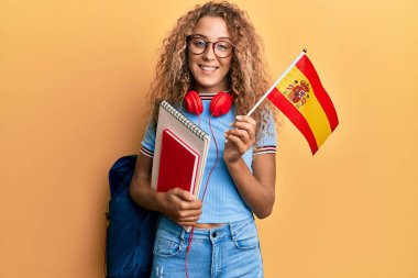 Güzel beyaz kız değişim öğrencisi elinde İspanyol bayrağı, yüzünde mutlu ve havalı bir gülümsemeyle gülümsüyor. diş gösterme. 