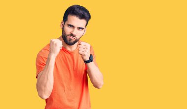 Sakallı, sıradan tişörtlü, yumruk savunma hareketleriyle dövüşmeye hazır, sinirli ve üzgün yüzlü, problemden korkan genç yakışıklı bir adam. 