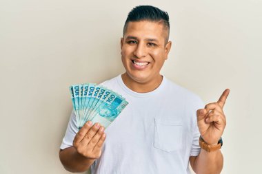 Genç Latin adam elinde 100 Brezilyalı gerçek banknot tutarken mutlu bir şekilde gülümsüyor. 
