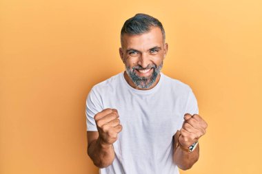 Orta yaşlı beyaz tişört giyen yakışıklı bir adam başarıya ulaşacağı için heyecanlı kolları havada ve gözleri kapalı zaferi kutlarken gülümsüyor. Kazanan konsept. 