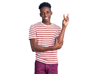 Genç Afro-Amerikalı sıradan kıyafetler giyen, gülen yüzlü, kameraya göz kırpan zafer işareti yapan genç bir adam. İki numara.. 