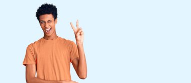 Genç Afro-Amerikalı sıradan kıyafetler giyen, gülen yüzlü, kameraya göz kırpan parmaklarıyla zafer işareti yapan genç bir adam. İki numara.. 