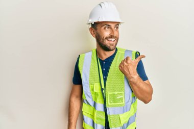 Sakallı, kasklı ve parlak ceketli yakışıklı bir adam baş parmağını yukarı kaldırıyor ve ağzı açık gülümsüyor. 