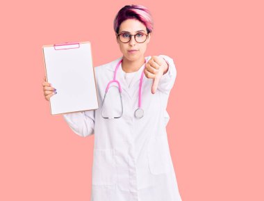 Young beautiful woman with pink hair wearing doctor stethoscope holding clipboard with medical report with angry face, negative sign showing dislike with thumbs down, rejection concept 