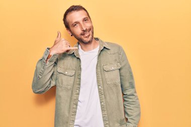 Genç, yakışıklı, sıradan kıyafetler giymiş, gülümseyen, el ve parmaklarıyla telefonla konuşan bir adam. iletişim kavramları. 