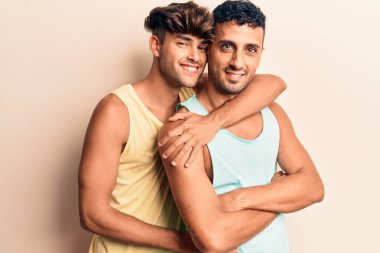 Yazlık kıyafetler giyen genç bir çift mutlu gülümsüyor. Yüzünde gülümsemeyle dikilip izole edilmiş beyaz arka planda sarılıyorum.