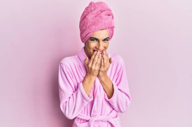 Kadın elbisesi giyen genç adam makyaj havlusu ve bornoz giyerek gülüyor ve utanarak kıkırdıyor elleri, dedikoduları ve skandalları ağızlarına tıkıyor. 