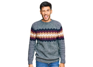 Kış süveteri giyen genç yakışıklı bir adam kameraya seksi bir ifadeyle bakıyor, neşeli ve mutlu bir yüzle.. 