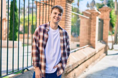 Genç beyaz adam gülümseyerek şehirde mutlu mesut duruyor..