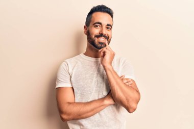 Gündelik giysiler giyen genç İspanyol adam kameraya kollarını kavuşturup çenesine dokunarak gülümsüyor. Olumlu düşünmek. 