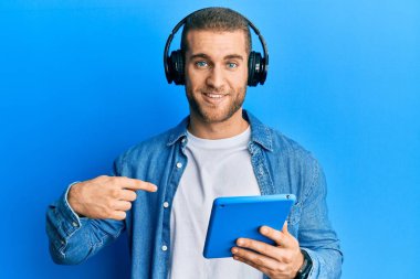 Kulaklık takmış, dokunmatik ped kullanan genç beyaz bir adam gülümseyen ve gururlu birini işaret ediyor. 