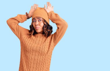 Yün kazak giyen, kışlık şapkalı, tavşan kulağı takan genç ve güzel melez bir kadın avuç içi hareketleriyle alaycı ve şüpheci görünüyor. Paskalya tavşanı konsepti. 