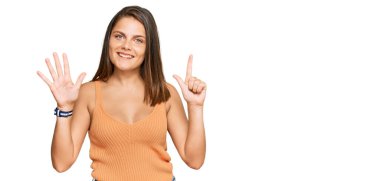 Gündelik giysiler giyen genç beyaz kadın yedi numarayı gösterip işaret ederken kendinden emin ve mutlu bir şekilde gülümsüyor.. 