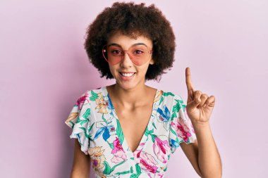 Yaz tarzı giyinen genç İspanyol kız ve bir fikirle gülümseyen güneş gözlükleri duyuyor ya da mutlu yüzle işaret eden bir soru işareti, bir numara. 