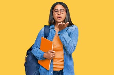 Genç Latin kız öğrenci çantası takıyor ve elinde kitaplarla kameraya bakıyor. Havadan öpücükler savuruyor. Güzel ve seksi. aşk ifadesi. 