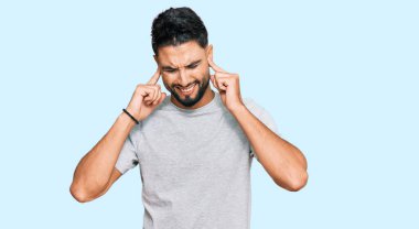 Gri tişörtlü, sakallı genç adam yüksek sesli müzik sesi için kulaklarını parmaklarıyla kapatıyor. sağır kavramı. 