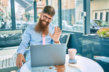Genç kızıl saçlı işadamı, kahve dükkanının terasında dizüstü bilgisayarla video görüşmesi yapıyor..