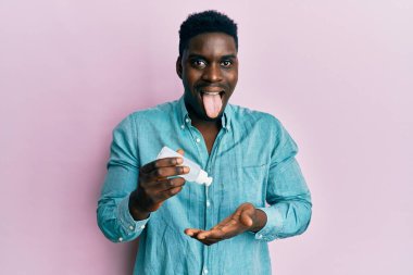 Yakışıklı siyah adam el dezenfektanı jeli kullanıyor. Dilini çıkartıyor. Komik bir ifadeyle mutlu.. 