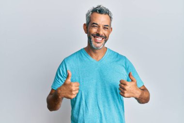 Orta yaşlı, gri saçlı, günlük kıyafetler giyen, başarı işareti takan, elinde olumlu bir jest yapan, gülümseyen ve mutlu bir adam. Neşeli ifade ve kazanan jest. 