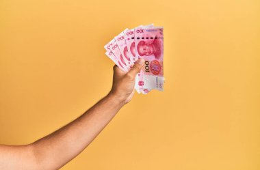 Çin malı 100 Yuan 'lık banknotları izole edilmiş sarı arka planda tutan İspanyol adamın eli..