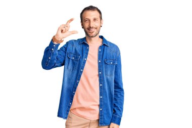 Gündelik kıyafetler giyen, gülümseyen, kendine güvenen, el hareketleriyle küçük boy işareti yapan, parmaklarıyla işaret eden ve kameraya bakan genç yakışıklı bir adam. ölçüm kavramı. 