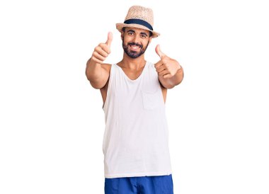 Gündelik yaz şapkası takan İspanyol genç adam elinle olumlu jest yapmayı onaylıyor, gülümsüyor ve başarı için mutlu. kazanan jest. 