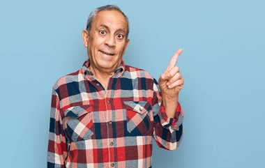 Kıdemli İspanyol adam gündelik kıyafetler giyip gülümsüyor mutlu bir şekilde elini ve parmağını yana doğru gösteriyor. 