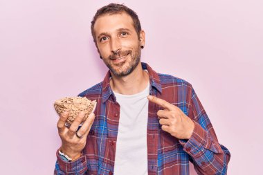 Genç yakışıklı adam mısır gevreği tutuyor gülümsüyor mutlu bir şekilde eli ve parmağı ile işaret ediyor. 